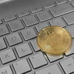 A physical bitcoin resting on a laptop keyboard.