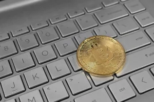A physical bitcoin resting on a laptop keyboard.