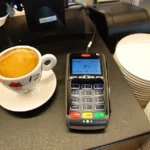 A card payment terminal on a cafe counter next to a cup of coffee.