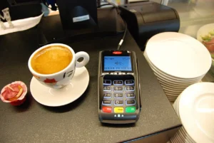 A card payment terminal on a cafe counter next to a cup of coffee.